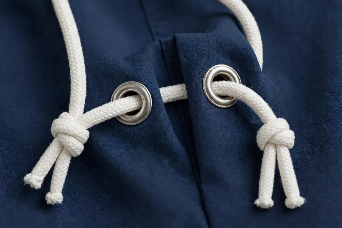 Close-up of a white drawstring knotted through metal eyelets on navy swim-short fabric